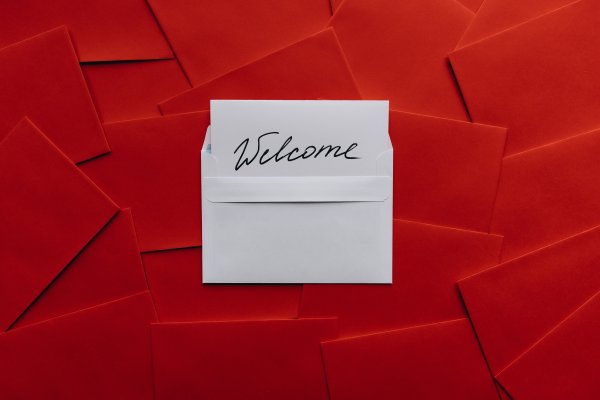 White card & envelope with Welcome written on it, laying on pile of red envelopes