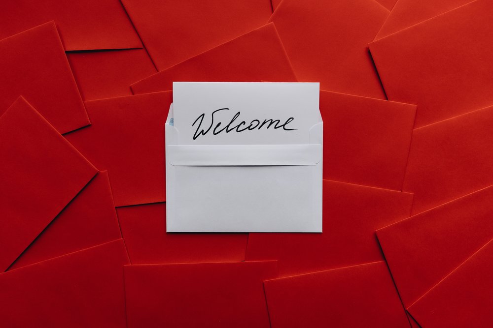 White card & envelope with Welcome written on it, laying on pile of red envelopes